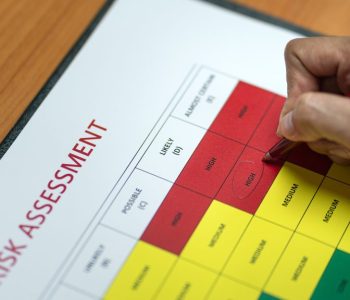 Action of a person is using ballpoint pen to marking on the risk assessment matrix table at "High risk" level. Industrial or business working action scene photo. Close-up and selective focus.